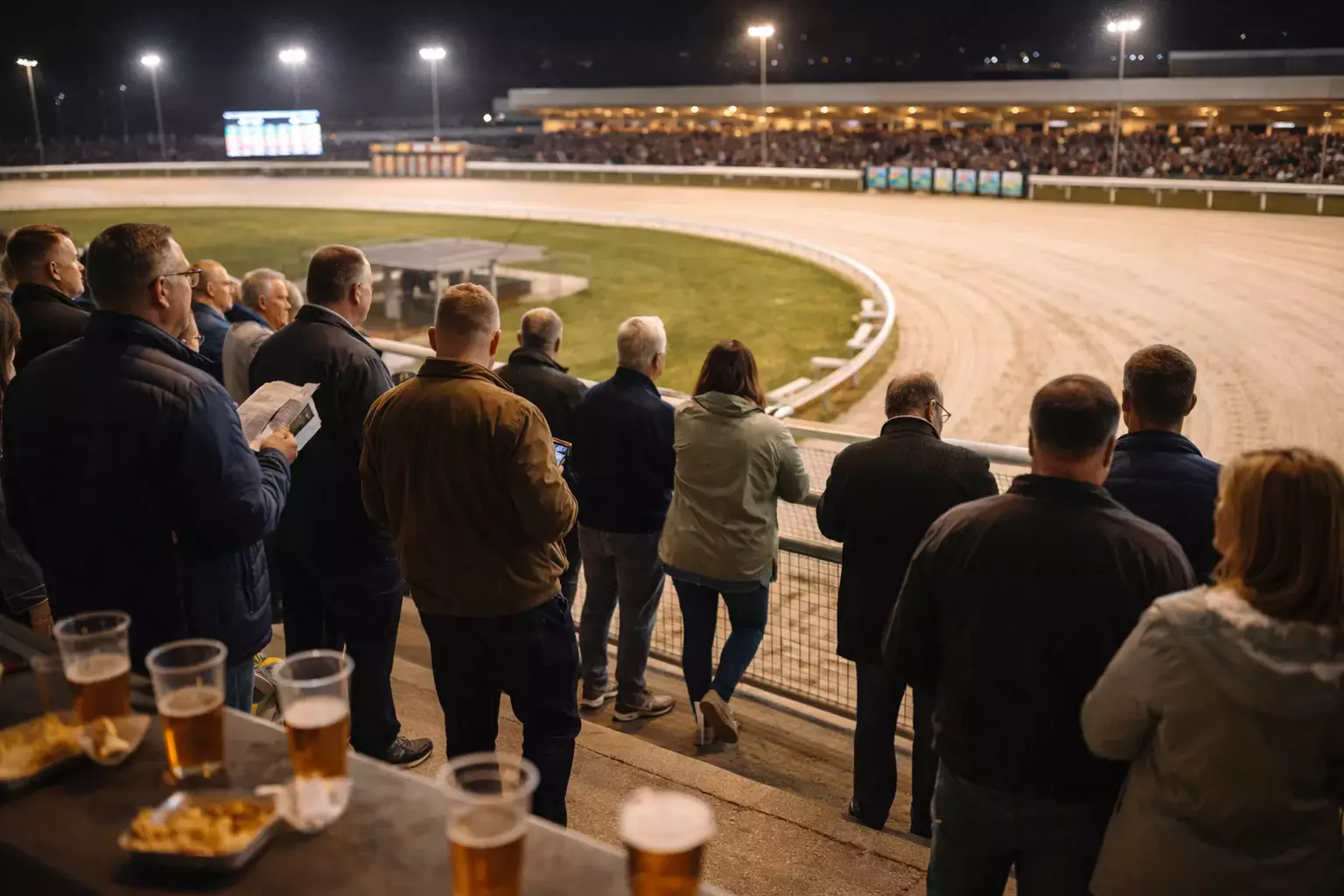 Spectators watching greyhound racing from terraces at a UK stadium during an evening meeting