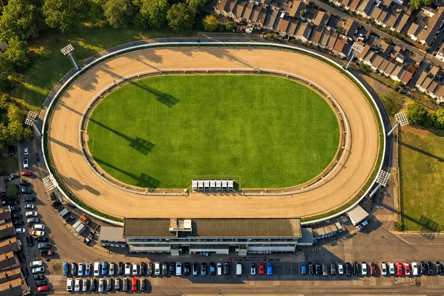 Aerial view of an oval greyhound racing track with sand surface and floodlight towers